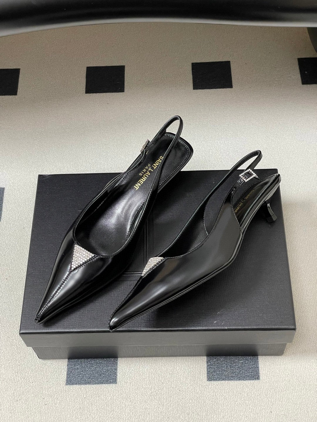 Saint Laurent Cherish 30 slingback pumps in black glazed calfskin leather with a rhinestone triangle detail